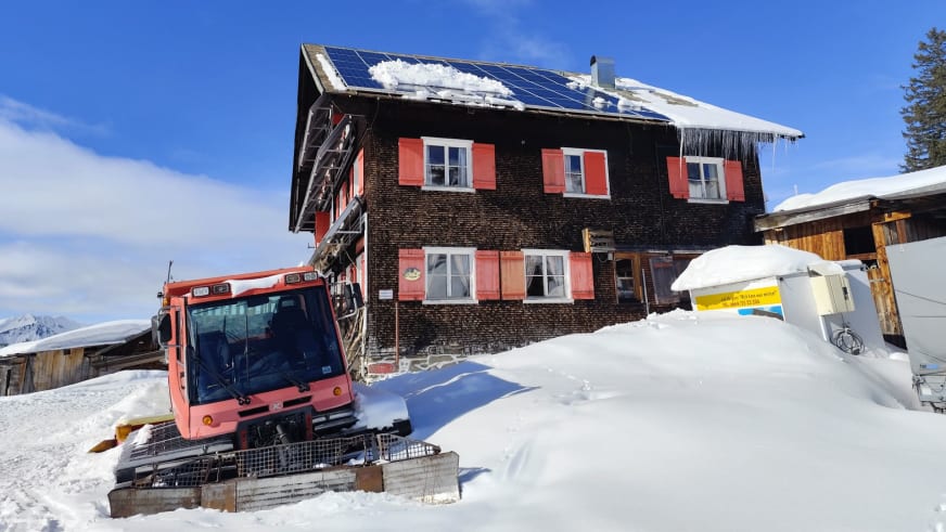 Das Neuhornbachhaus auf 1700 m mit traditioneller Holzfassade und roter Pistenraupe im verschneiten Gelände.