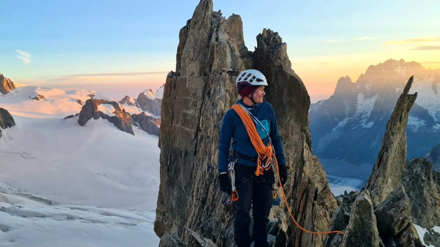 Auf einem schmalen Felsvorsprung steht Bergwanderführerin Magdalena Strötz mit Kletterausrüstung vor vergletscherter Hochgebirgslandschaft.