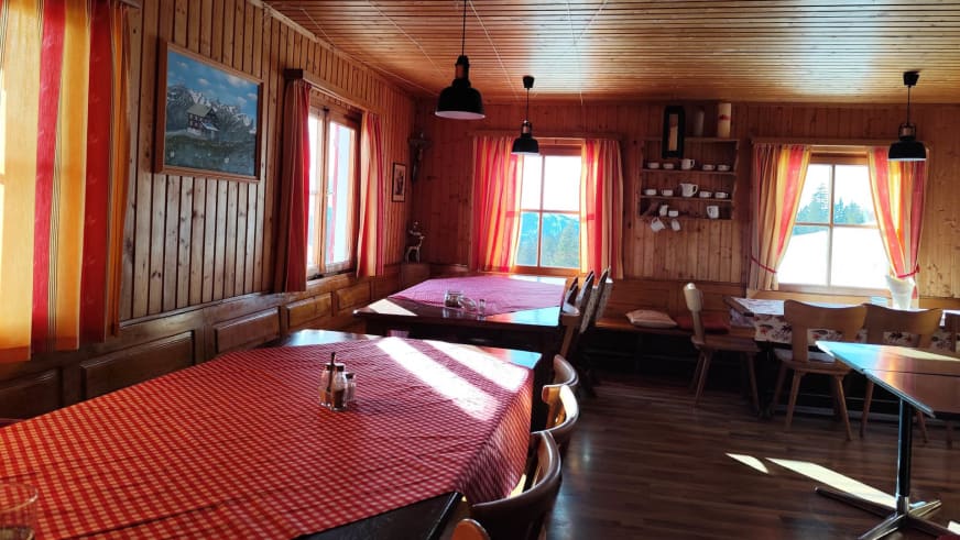 Holzvertäfelter Gastraum im Neuhornbachhaus mit rot-weißen Tischdecken und Blick auf die bewaldete Berglandschaft.