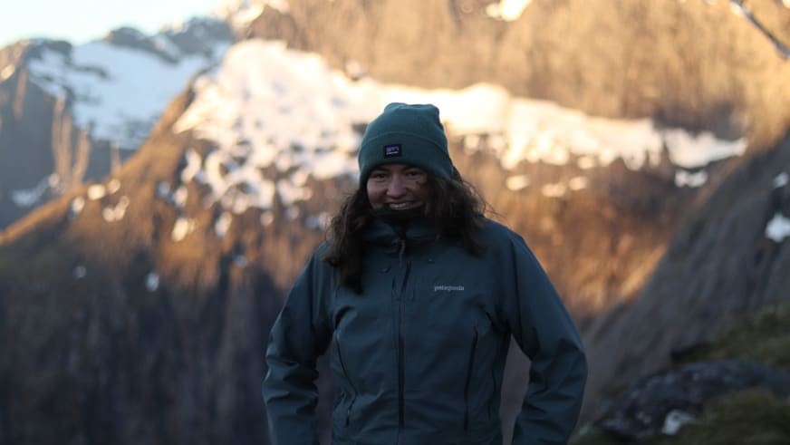 Portrait der Bergwanderführerin Magdalena Strötz mit grüner Strickmütze und blauer Outdoorjacke vor schneebedeckten Gipfeln.
