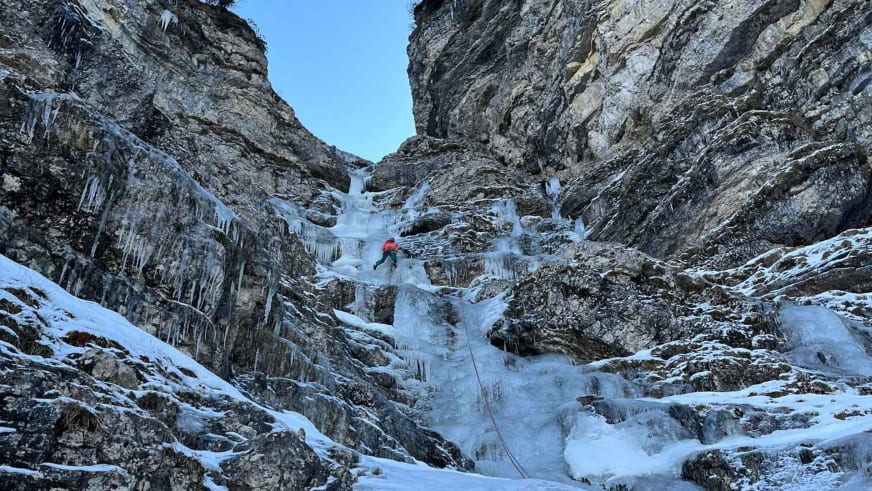 Bergführerin Monika Hümmer in roter Kleidung klettert an gefrorenem Wasserfall mit Eiszapfen.