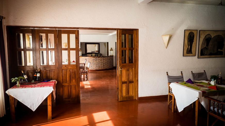 Gedeckte Holztische und Backsteinlamin im Gastraum der Ilboru Safari Lodge bei Arusha.