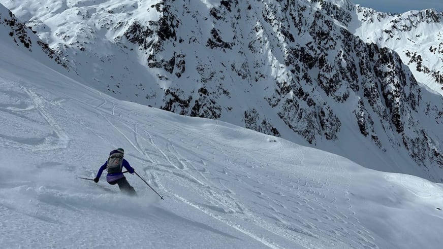 Bergführerin Monika Hümmer fährt in violetter Jacke durch Pulverschnee vor Bergkulisse.