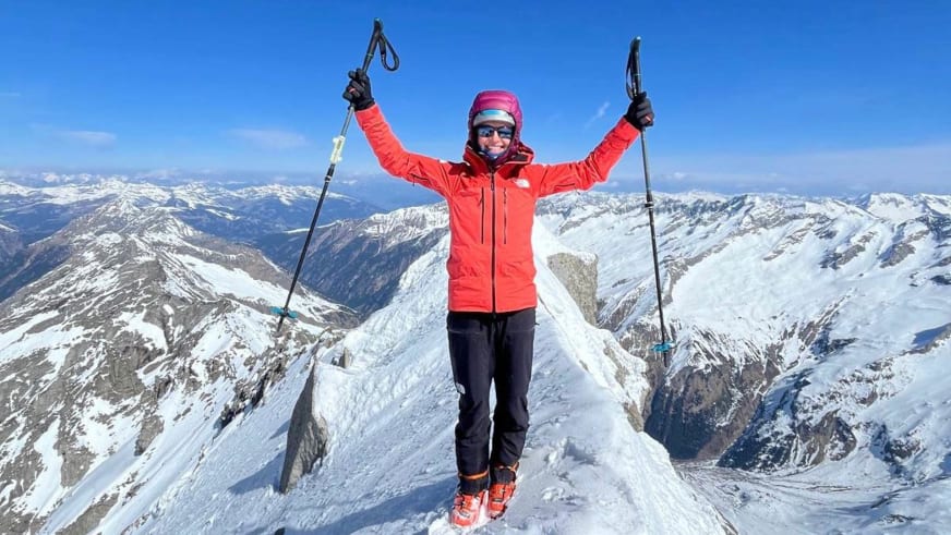 Bergführerin Monika Hümmer jubelt mit erhobenen Skistöcken auf verschneitem Gipfelgrat.