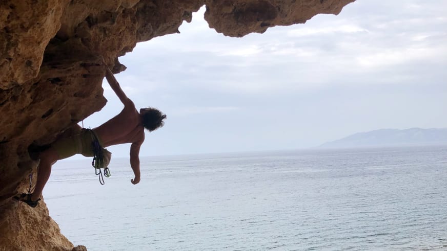Am überhängenden Kalkfels über dem Meer klettert Bergführer Christoph Vonmetz mit Klettergurt und Chalkbag.