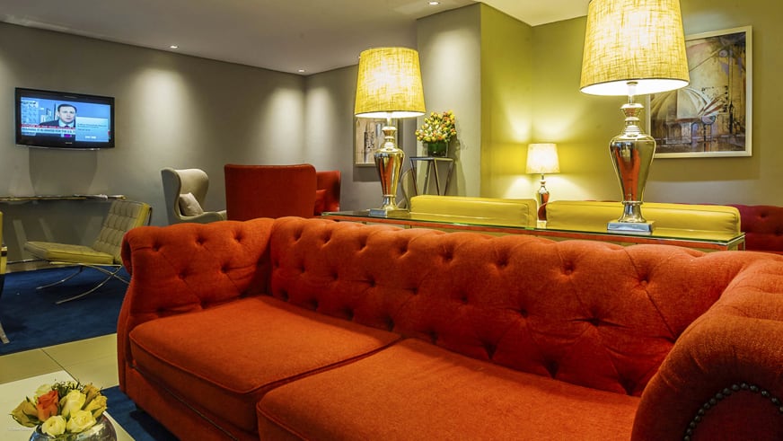 Hotel-Lounge im Eka Hotel mit großem orangefarbenem Sofa, gelben Stehlampen und verschiedenen Sesseln.