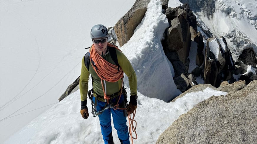 Bergführer Wolfgang Wagner steht mit orangem Kletterseil und grauem Helm auf schneebedecktem Grat in hochalpinem Gelände.
