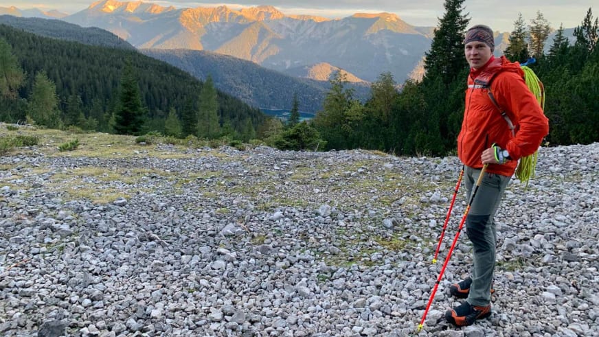 Mit roten Wanderstöcken und Stirnlampe steht Bergführer Wolfgang Wagner im Geröllfeld vor bewaldeter Alpenlandschaft.