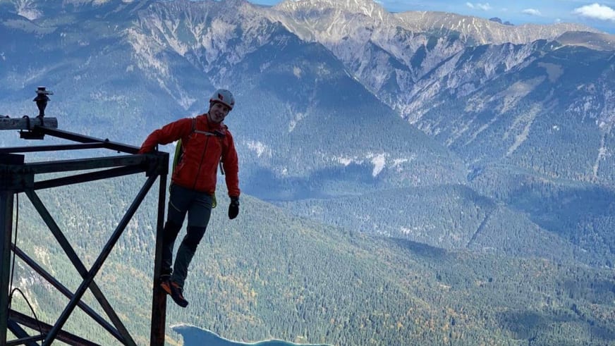 Bergführer Wolfgang Wagner in roter Jacke und weißem Helm steht auf schwarzer Stahlkonstruktion mit X-förmigen Verstrebungen.
