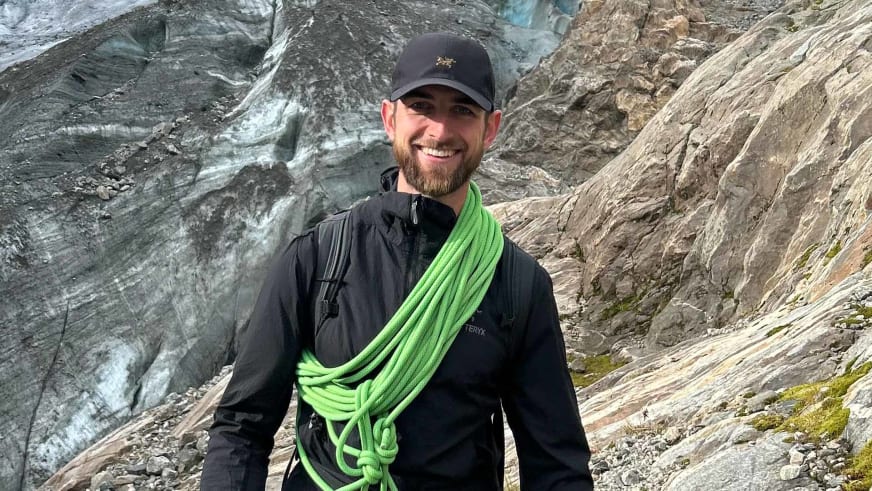 An einer hellen Felswand posiert Bergführer Joshua Wontroba mit grünem Kletterseil über der Schulter.