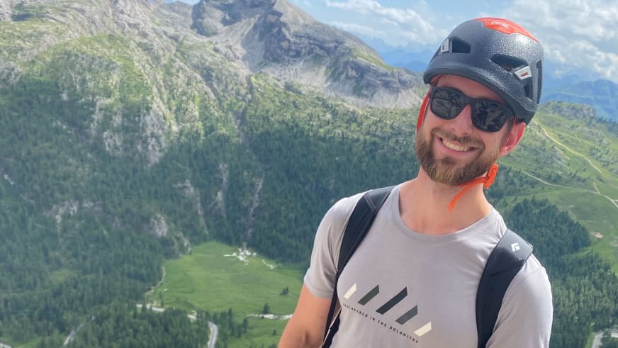 Portrait von Bergführer Joshua Wontroba mit schwarzem Kletterhelm vor weitläufiger Berglandschaft.