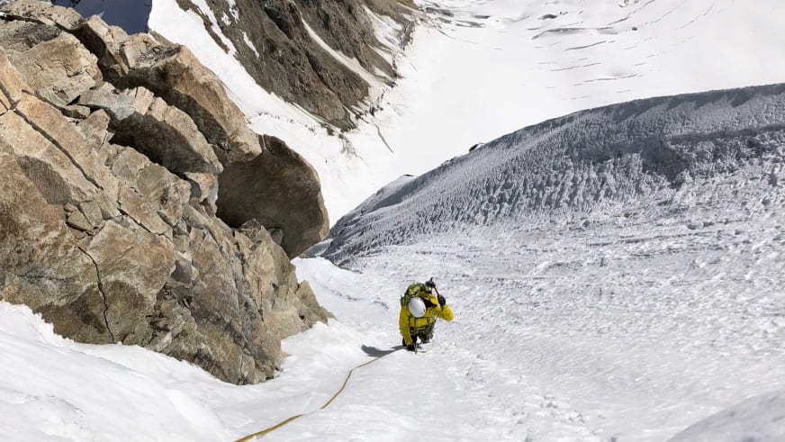 In gelber Winterbekleidung steigt Bergführer Simon Taffner einen steilen, verschneiten Hang hinauf, gesichert am Seil.