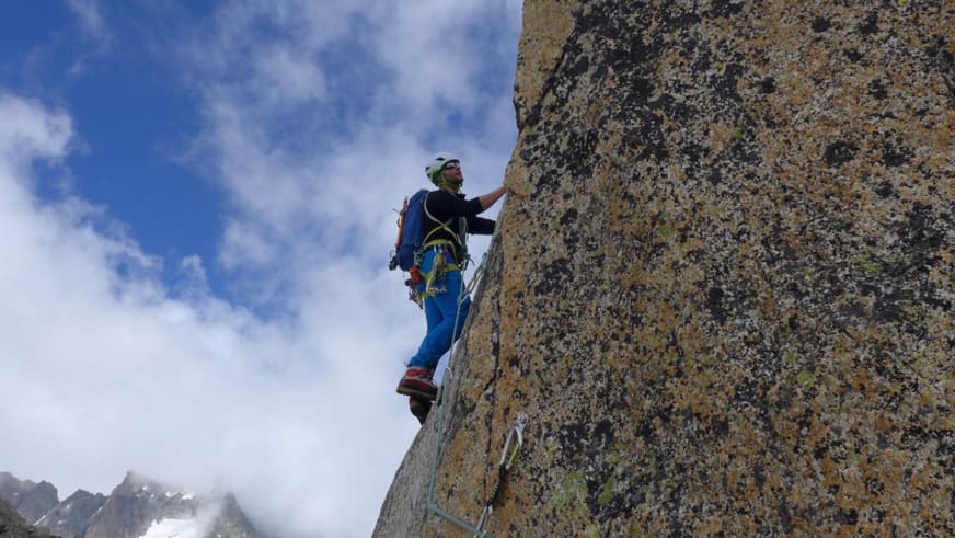 Bergführer Simon Taffner klettert in blauer Kleidung mit grünem Helm an einer steilen Felswand aus gelblich-grauem Gestein.