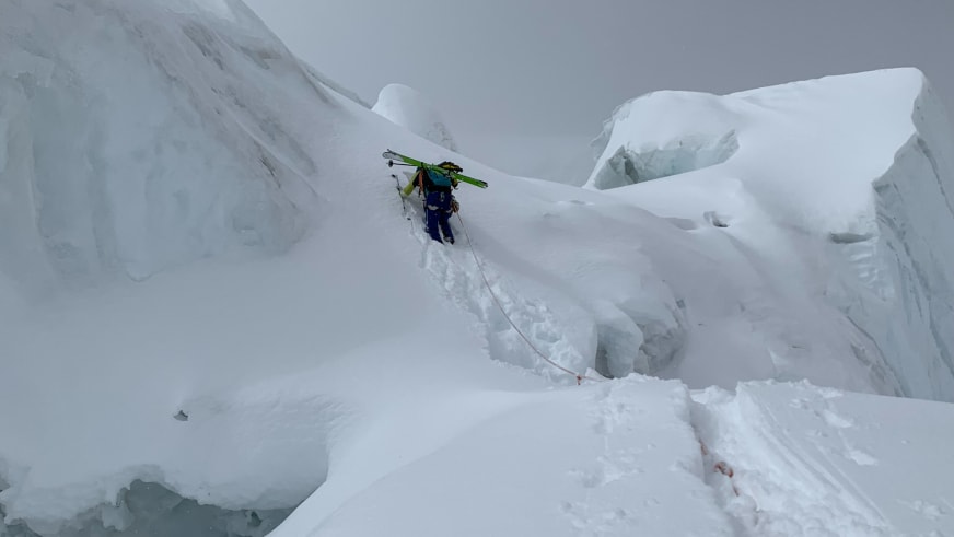 Mit grünen Skiern auf dem Rücken steigt Bergführer Simon Taffner durch zerklüftetes Gletscherterrain mit tiefen Spalten auf.