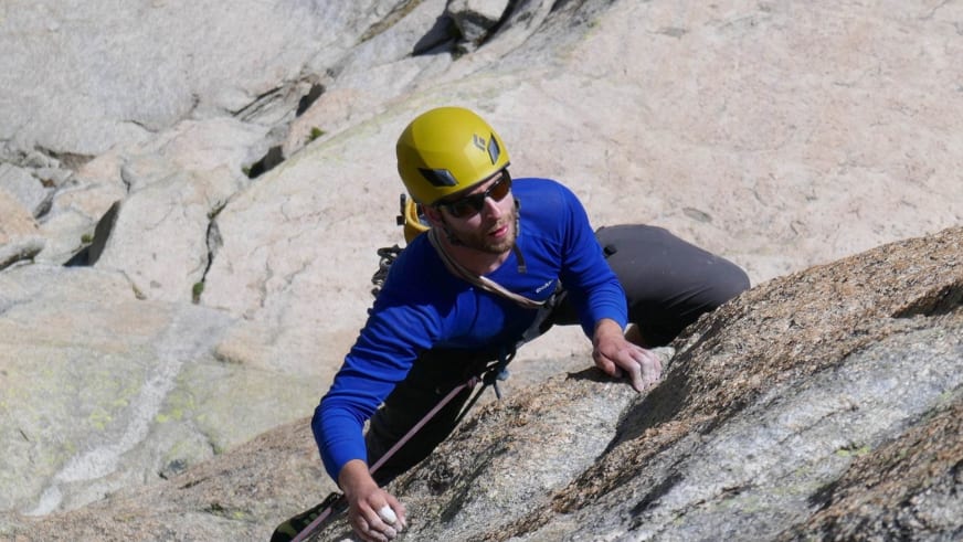 In blauem Langarmshirt und gelbem Kletterhelm greift Bergführer Simon Taffner nach Griffen an einer hellen Granitwand.