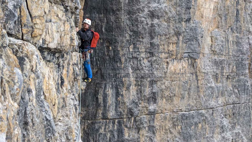 An grauer Kalksteinwand klettert Bergführer Christoph Meysel mit weißem Helm und Kletterausrüstung.