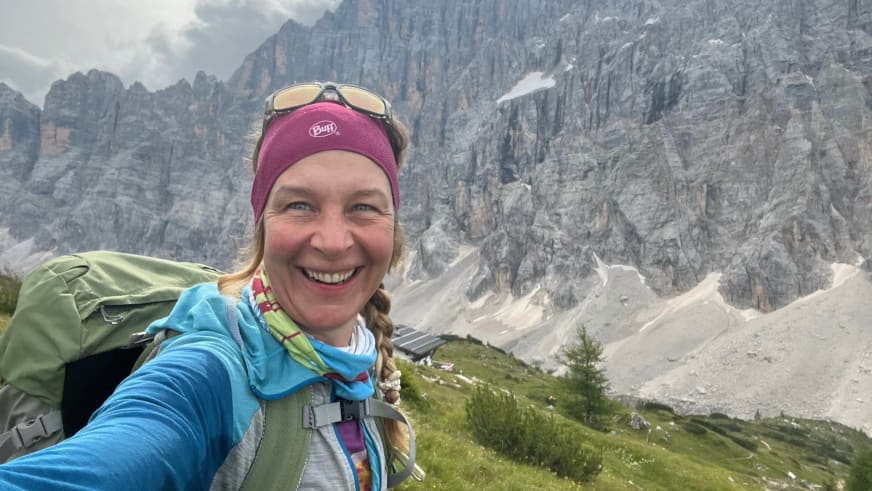 Selfie von Bergwanderführerin Bernadette Schnabl mit blonden Zöpfen, rotem Stirnband und blauer Jacke vor alpiner Felswand.