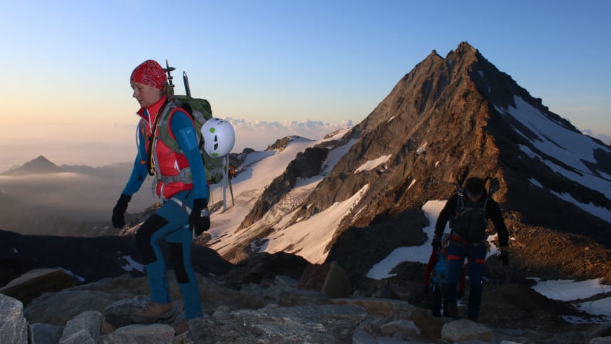 Bei goldenem Licht auf Hochtour bewegt sich Bergwanderführerin Bernadette Schnabl über felsiges Terrain mit weißem Helm in der Hand.