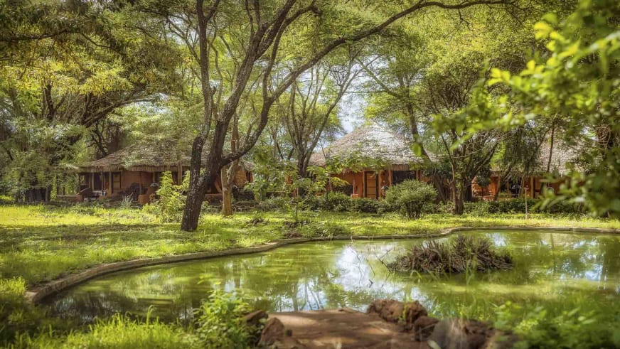 Gartenanlage der Amboseli Sopa Lodge mit rechteckigem Pool und traditionellen Rundbauten mit Strohdächern.