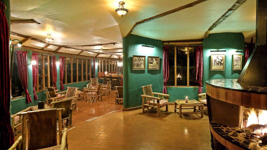 Hemingway Bar in der Amboseli Sopa Lodge mit brennendem Kamin, Holztischen und rustikalem Ambiente.