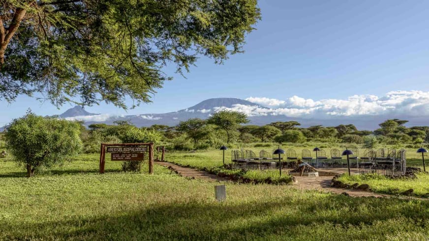 Eingangsbereich der Amboseli Sopa Lodge mit Holzschild und Kilimandscharo im Hintergrund der Akazien-Savanne.