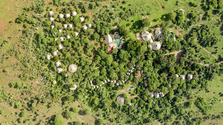 Luftaufnahme der Amboseli Sopa Lodge zeigt die Hauptgebäude, den Pool und die runden Bungalows mit Strohdächern.