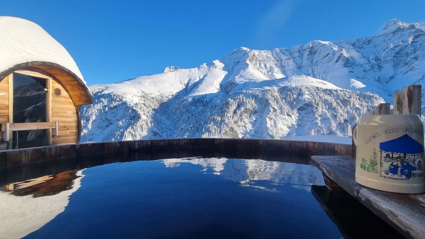 Außenpool mit Sauna-Tonne am Hotel Camana vor verschneiter Bergkulisse der Adula-Alpen bei Sonnenschein.