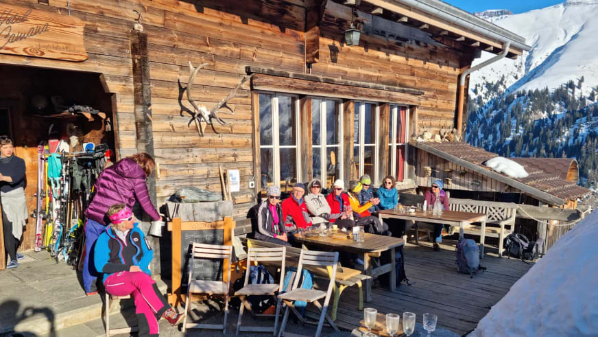 Skitourengeher pausieren auf der Sonnenterrasse des Hotel Camana bei strahlendem Wetter in bunter Winterkleidung.