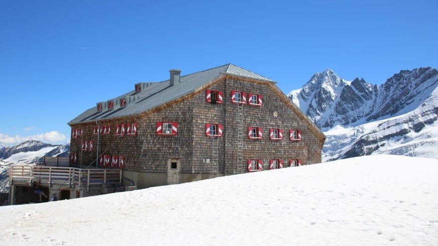 Winteransicht der Oberwalder Hütte aus Naturstein mit schneebedeckten Gipfeln der Hohen Tauern im Hintergrund.
