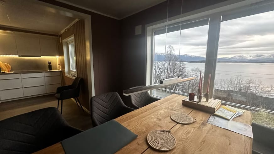 Wohn-Essbereich im Lyngen Blue House mit Holztisch und Panoramablick auf den verschneiten Fjord.