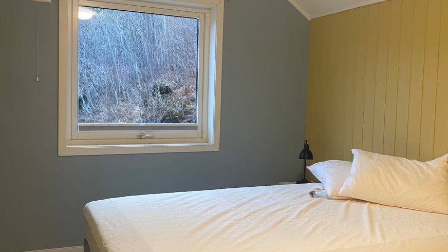 Schlafzimmer im Lyngen Blue House mit Doppelbett und Fenster zum bewaldeten Hang.