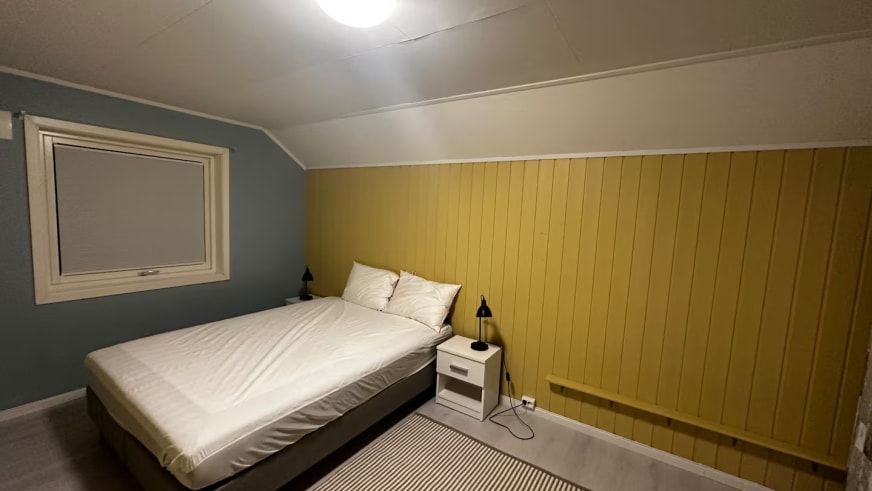 Dachzimmer im Lyngen Blue House mit weißer Holzverkleidung und Doppelbett.