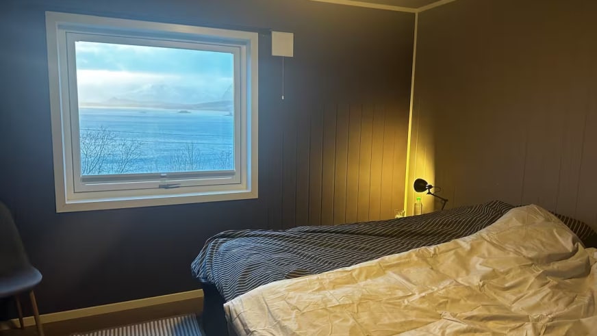Schlafzimmer im Lyngen Blue House mit großem Fenster und direktem Blick auf den Fjord.