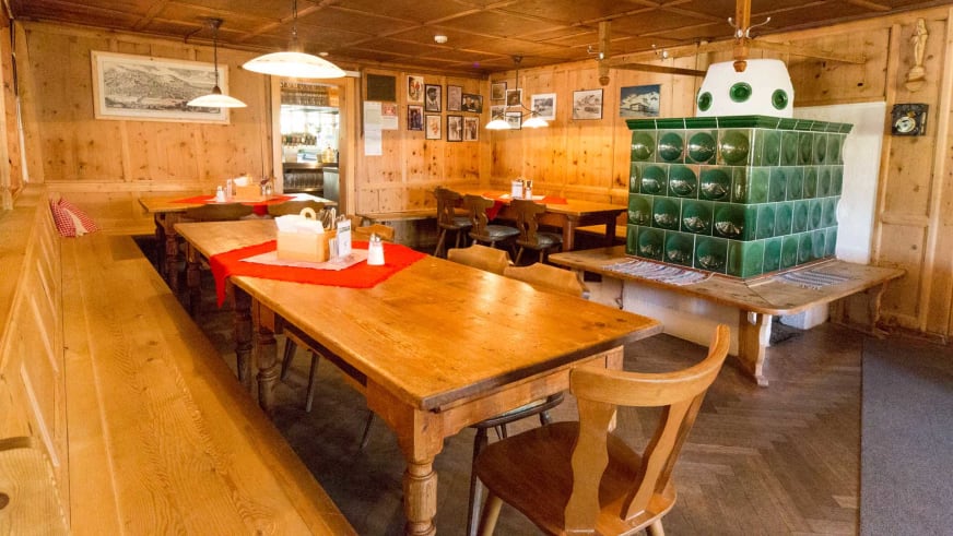 Gemütlicher Gastraum in der Heidelberger Hütte mit traditioneller Holzausstattung und grünem Kachelofen.