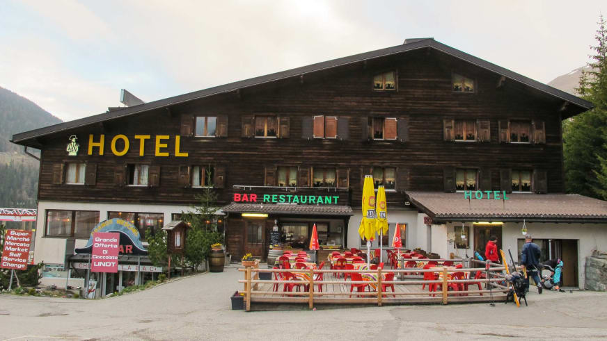 Das Hotel Bourg St Pierre zeigt seine traditionelle Holzfassade mit Restaurant-Terrasse und roten Gartenstühlen im Saint
