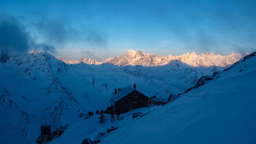 Die Cabane de Valsorey steht verschneit auf einem Felssockel während der blauen Stunde im Walliser Hochgebirge.