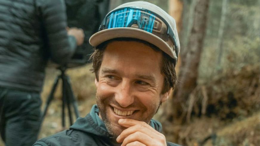 Bergführer Christian Brüderl lächelt freundlich in die Kamera und trägt eine türkise Softshell-Jacke mit Baseballkappe.