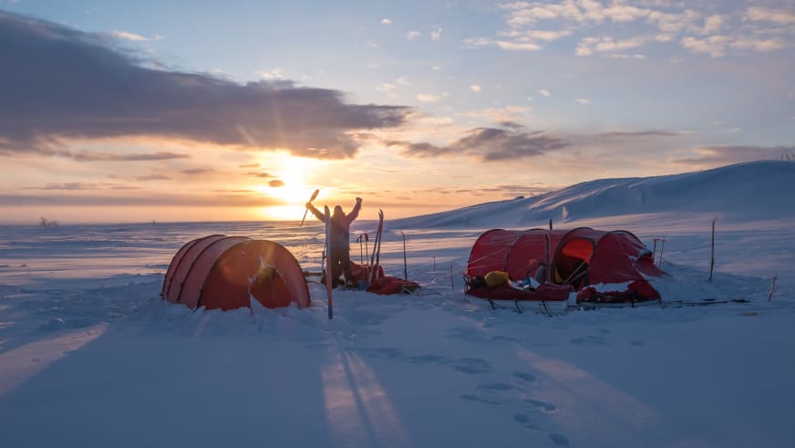 Bei Sonnenuntergang steht Bergwanderführer Mark Renker zwischen zwei roten Expeditionszelten im tiefen Schnee.