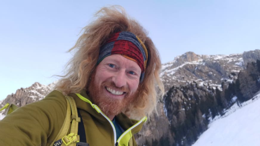 Bergführer Roland Wimmer macht ein Selfie vor schneebedeckten Felswänden in winterlicher Gebirgslandschaft.