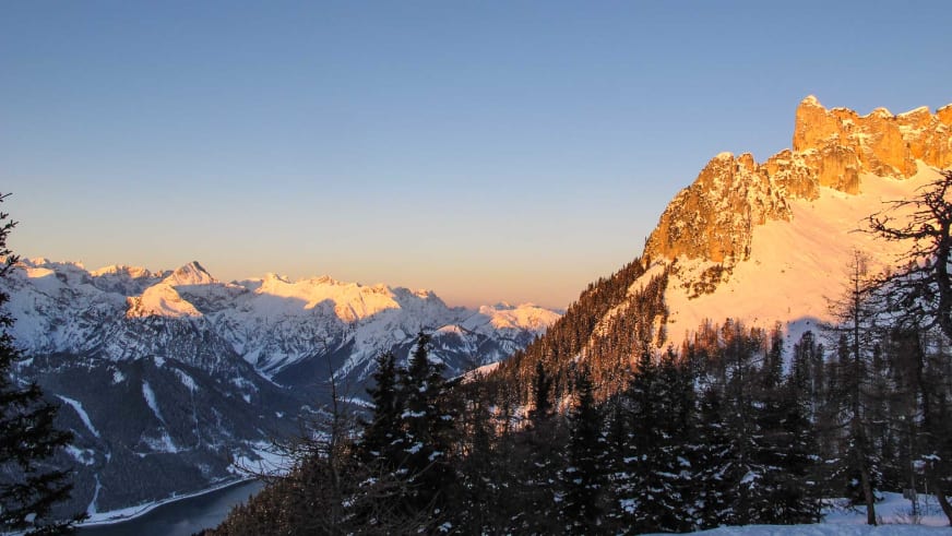 Blick von der Erfurter Hütte über verschneite Wälder auf die Bergketten des Rofangebirges.