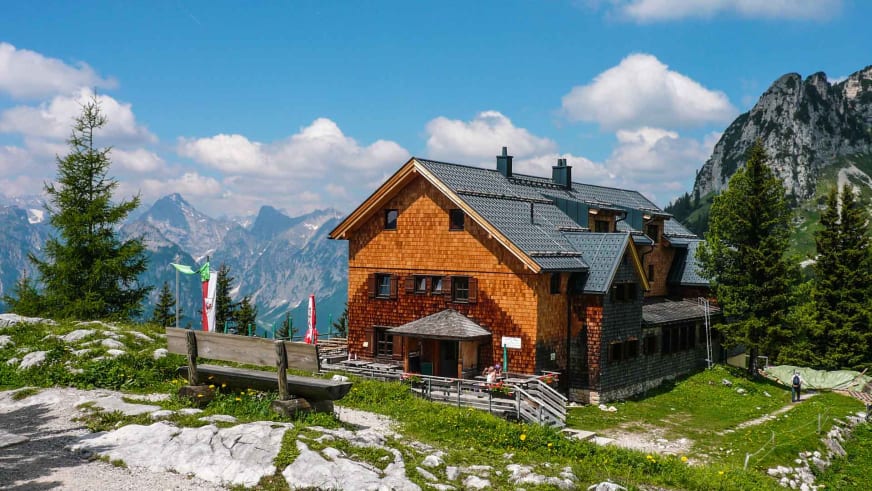 Die Erfurter Hütte mit traditioneller Holzfassade steht auf grüner Almwiese vor Bergpanorama.