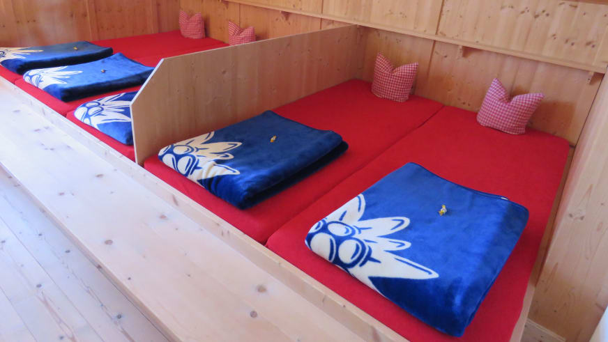 Matratzenlager in der Johannishütte mit roten Matratzen und blauen Schlafsäcken mit Edelweiss-Motiv.