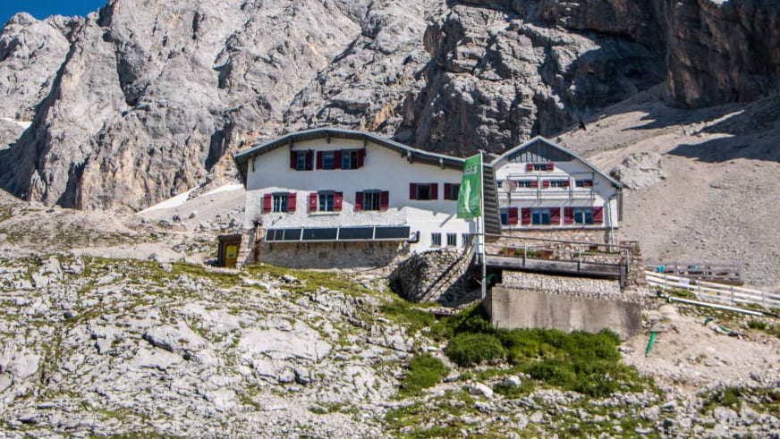 Gesamtansicht der Knorrhütte mit Haupt- und Nebengebäude vor den Felswänden des Zugspitzmassivs.