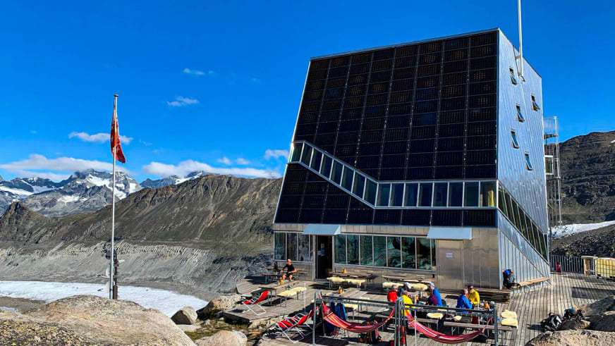 Wanderer entspannen auf der Terrasse der Monte Rosa Hütte mit Schweizer Flagge und Gletscherpanorama.