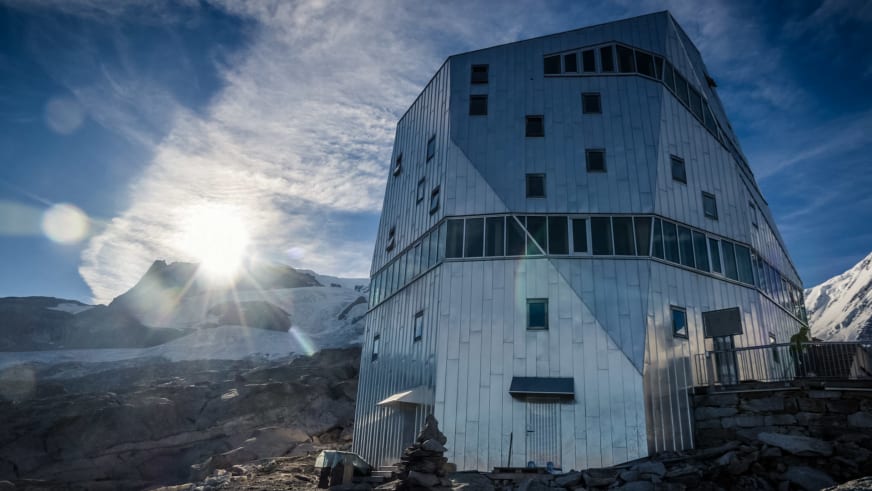 Die zylinderförmige Monte Rosa Hütte steht im Winter auf felsigem Gelände mit Gletscherblick.