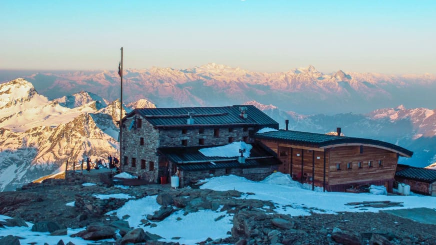 Mehrere Gebäudeteile des Rifugio Città di Mantova auf schneebedecktem Plateau während der Morgendämmerung.