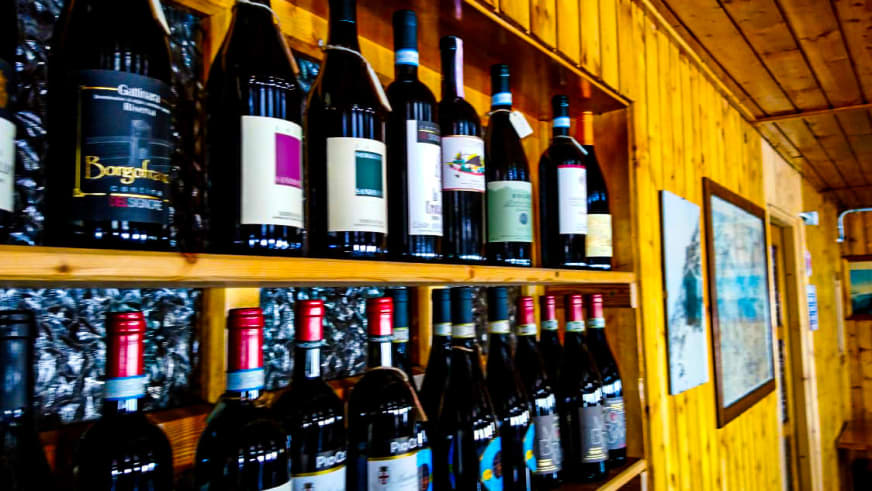 Weinregal mit verschiedenen Flaschen im Gastraum des Rifugio Città di Mantova mit Holzvertäfelung.