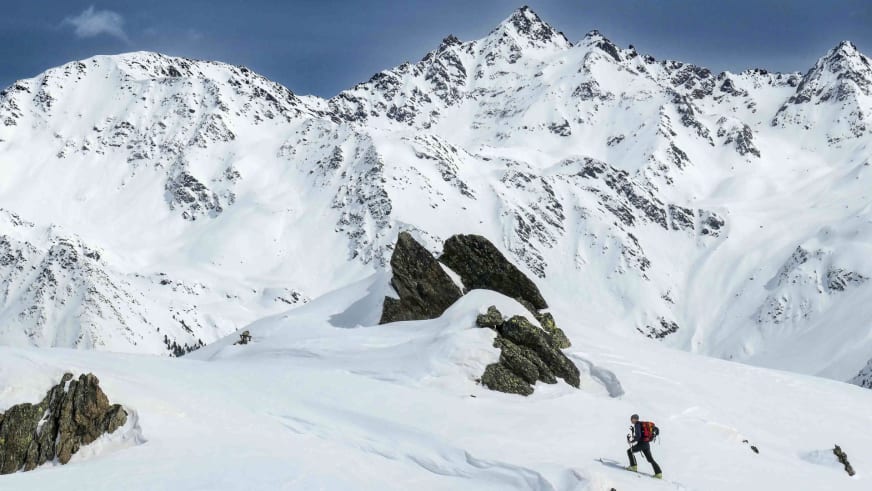 Skitourengeher mit rotem Rucksack auf verschneiter Hochfläche vor der Zufallhütte im Ortlergebiet mit Bergpanorama.