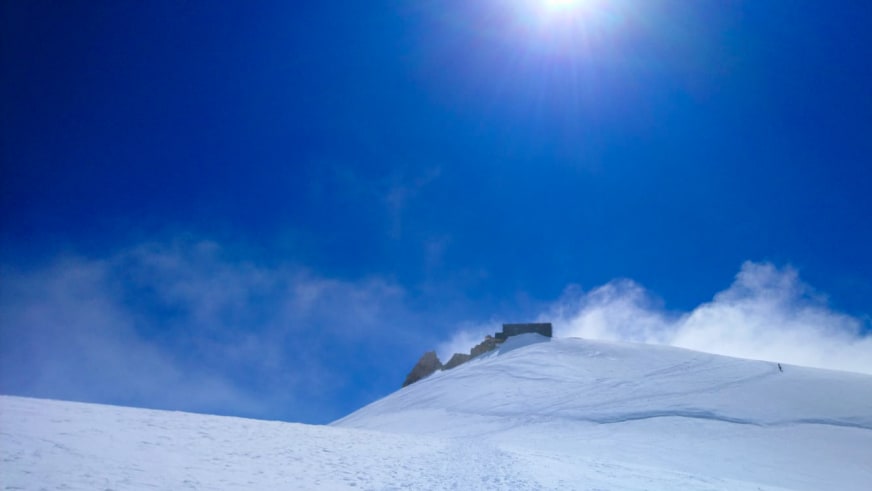 Winterpanorama zeigt die Capanna Margherita auf verschneitem Gipfelplateau unter tiefblauem Himmel.