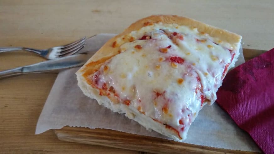 Frisch zubereitete Pizza wird auf weißem Teller in der Capanna Margherita serviert.